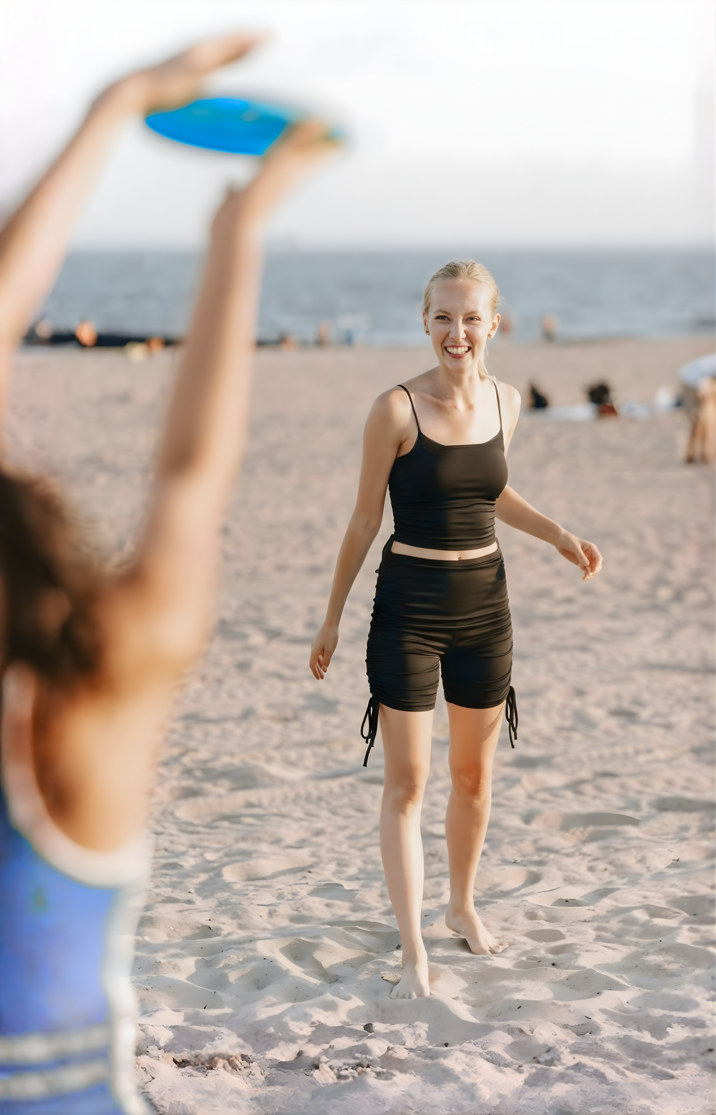 Une femme joyeuse et libre de ses mouvements jouant au frisbee sur la plage avec une amie. Elle porte un ensemble de bain semi-couvrant composé d'un top et d'un short de la marque Eclypse, lui permettant de faire du sport sereinement et sans gêne.