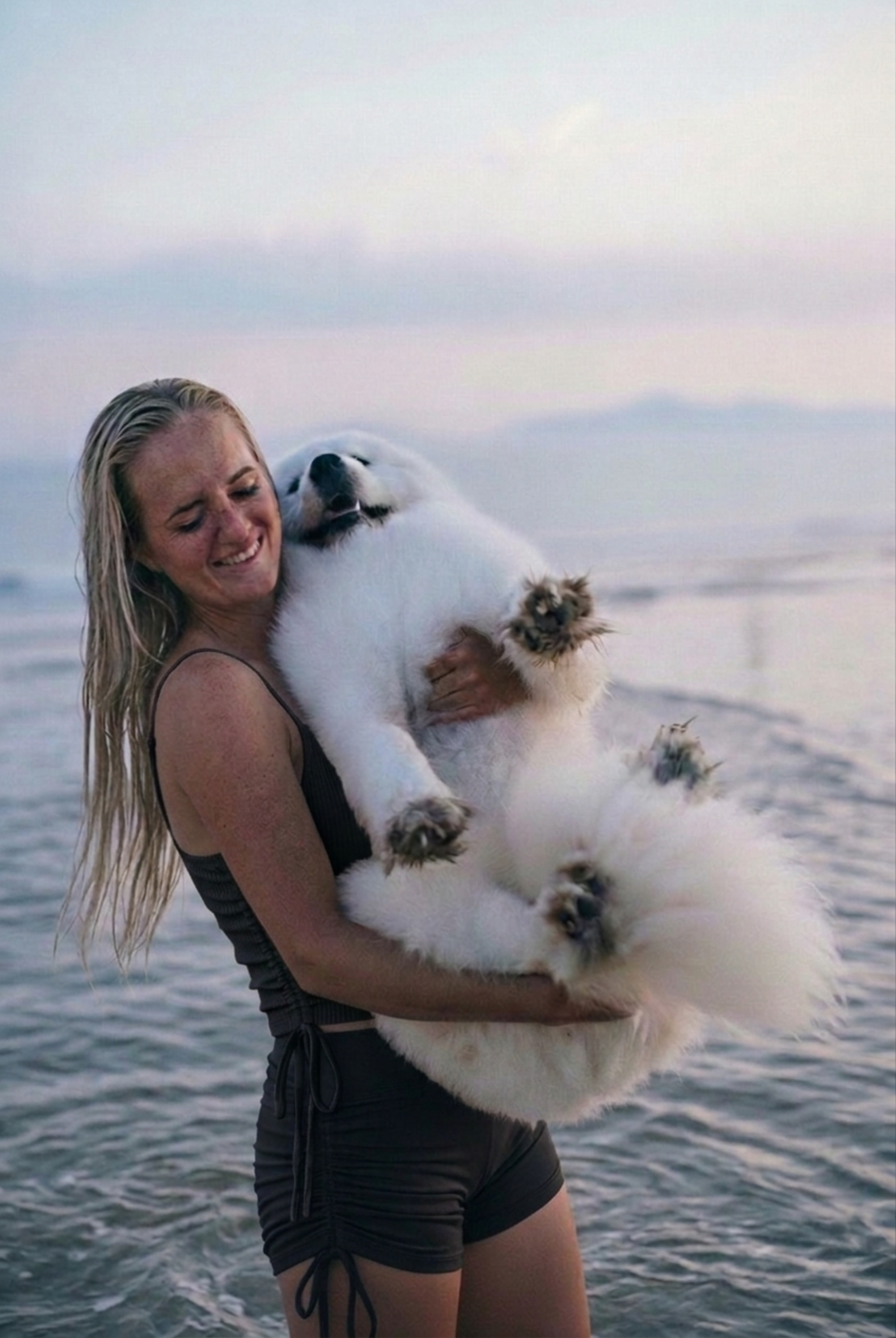 Une femme joyeuse fait son sport à la plage avec son chien. Elle porte son maillot de bain semi-couvrant Eclypse comme un vêtement de sport adapté à l'eau, car elle n'a pas peur de se baigner avec pour rejoindre son chien sans abîmer ou gêner par la suite. Image